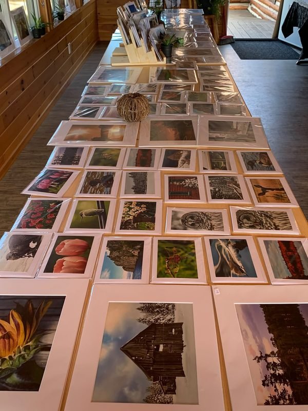 A long wooden table covered in sleeved photographic prints of many sizes, matted prints at the front
