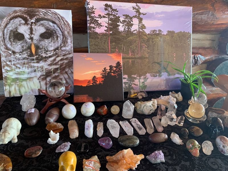 Canvas prints of a barred owl, a lake at dusk and a sunset, behind rows of crystals on black velvet